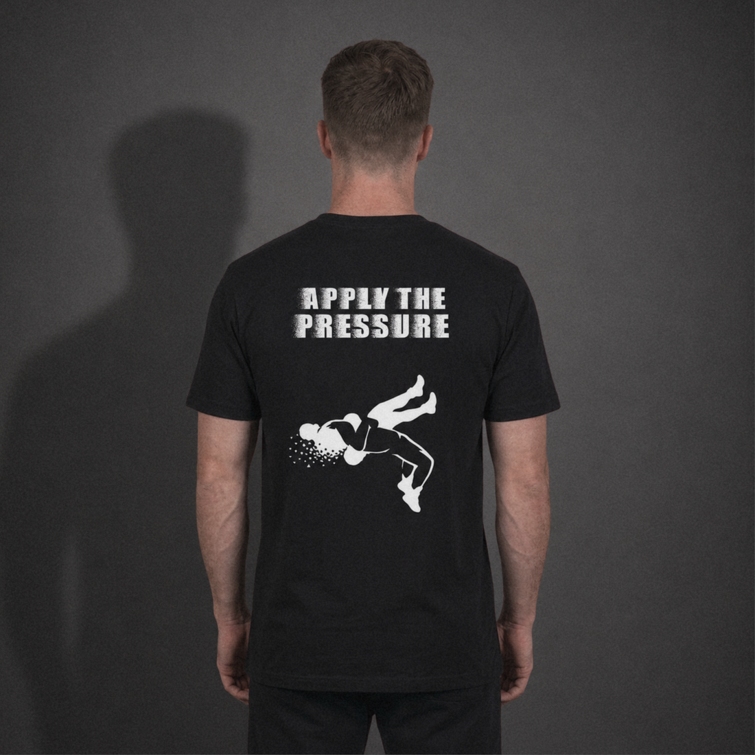 Back view of a grappler wearing the black Apply the Pressure Tee with a mid-throw wrestling graphic