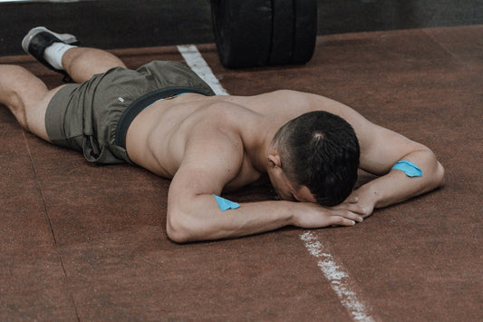 Athlete lying face down on the gym floor after a hard session, resting his head on his arms