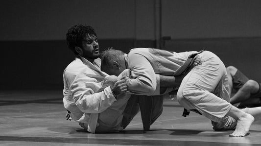 Black and white photo of a top player driving his head and chest into his partner with his hips low during a guard pass