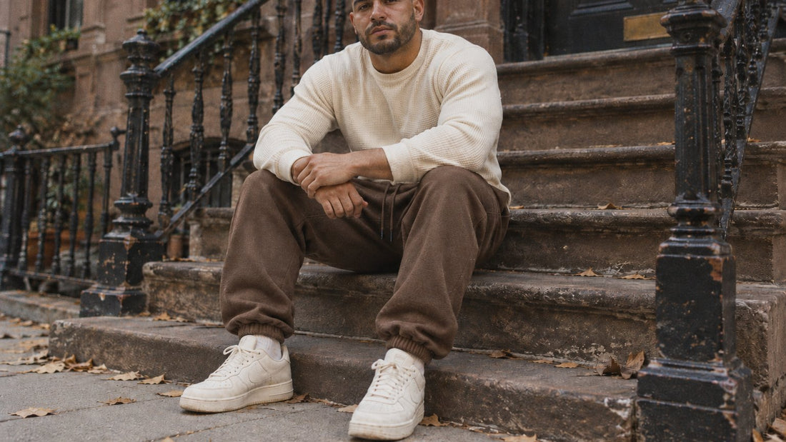 Man in a cream waffle sweater and brown Ranked Heavyweight Joggers sitting on a brownstone stoop in autumn