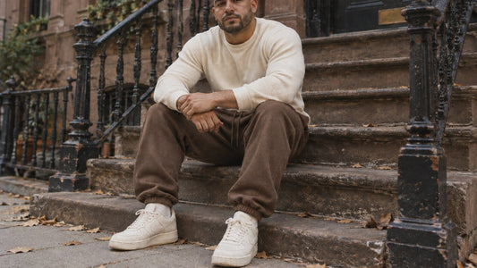 Man in a cream waffle sweater and brown Ranked Heavyweight Joggers sitting on a brownstone stoop in autumn