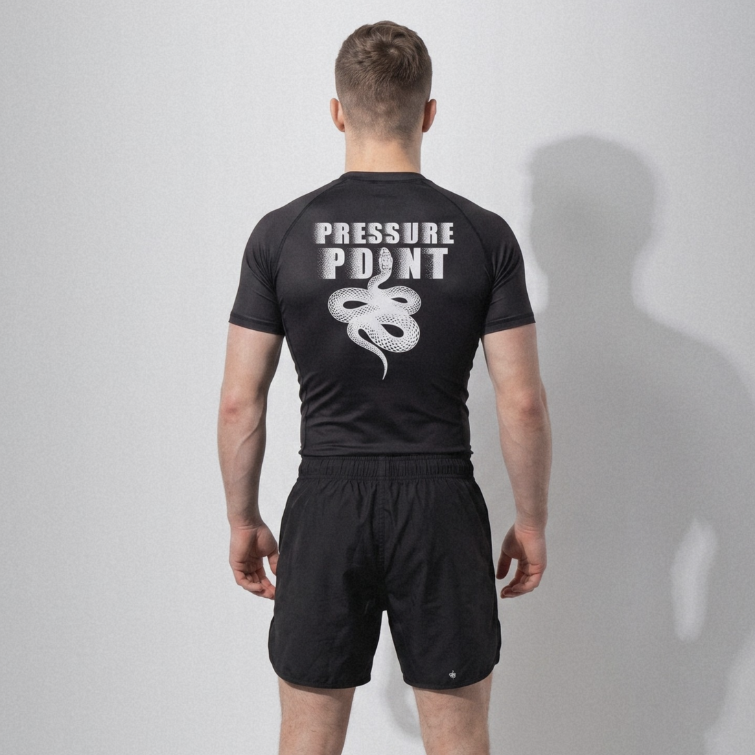 Grappler seen from behind in a black Pressure Point rashguard and black fight shorts, ready for no-gi class