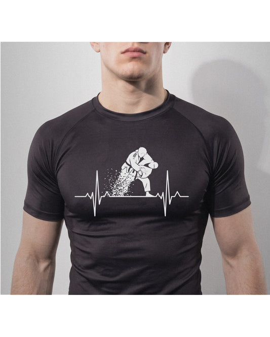 Grappler wearing the black Kuzushi Pulse Rashguard with a heartbeat line breaking into a jiu-jitsu throw across the chest