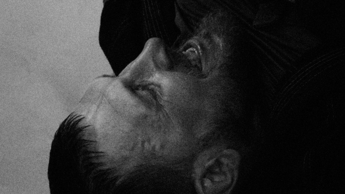Black-and-white close-up of a grappler pinned on the mat under a tight collar grip