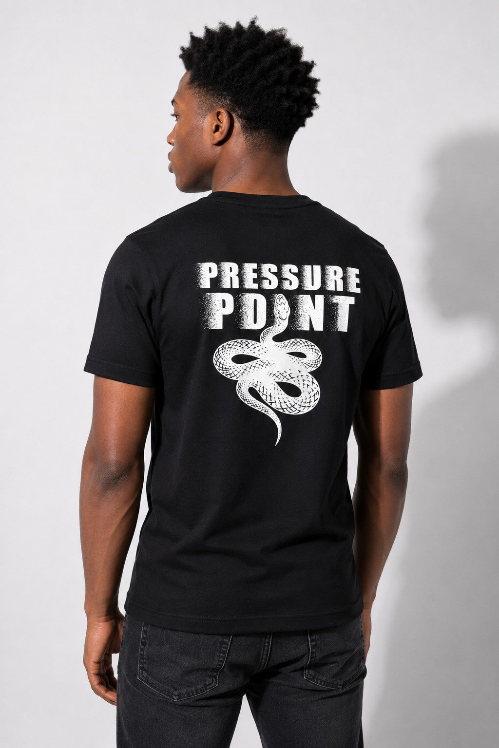 Back of the black Pressure Point tee on a model against a white wall