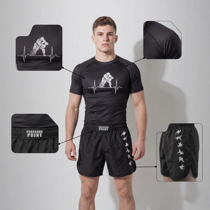 A man modeling a black short-sleeve rash guard and matching black shorts with white printed graphics, shown against a light gray studio background with four inset detail callouts pointing to the rash guard chest, sleeve, waistband, and shorts side. 